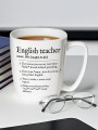 Kubek z herbatą i napisem „English teacher” z zabawną definicją, ustawiony na biurku obok okularów i stosu książek.