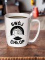 Porcelanowy kubek z czarnym nadrukiem przedstawiającym dwa splecione dłonie oraz napis „Swój chłop”, ustawiony na drewnianym blacie z warsztatem w tle.