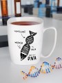 Biały kubek z nadrukiem DNA i hasłem „cierpliwość, wiedza, pasja - Mam to w DNA” stoi na biurku z probówkami i modelem DNA.