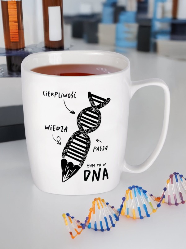 Biały kubek z nadrukiem DNA i hasłem „cierpliwość, wiedza, pasja - Mam to w DNA” stoi na biurku z probówkami i modelem DNA.