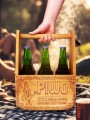 Drewniane nosidło na piwo z grawerem „Piwo – kto z sobą nosi, nikogo nie prosi” trzymane w ręce, w tle ognisko i piknik w plenerze.